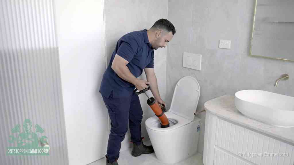 Een monteur buigt over een wandcloset en duwt met de hand een persluchtontstopper in de toiletpot om de verstopping handmatig los te maken in Emmeloord
