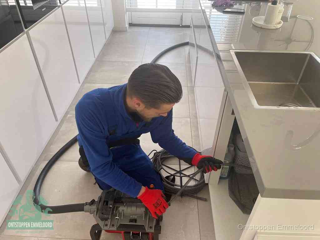 Een monteur ontstopt de keukenafvoer onder de spoelbak met een elektrische veermachine in Emmeloord