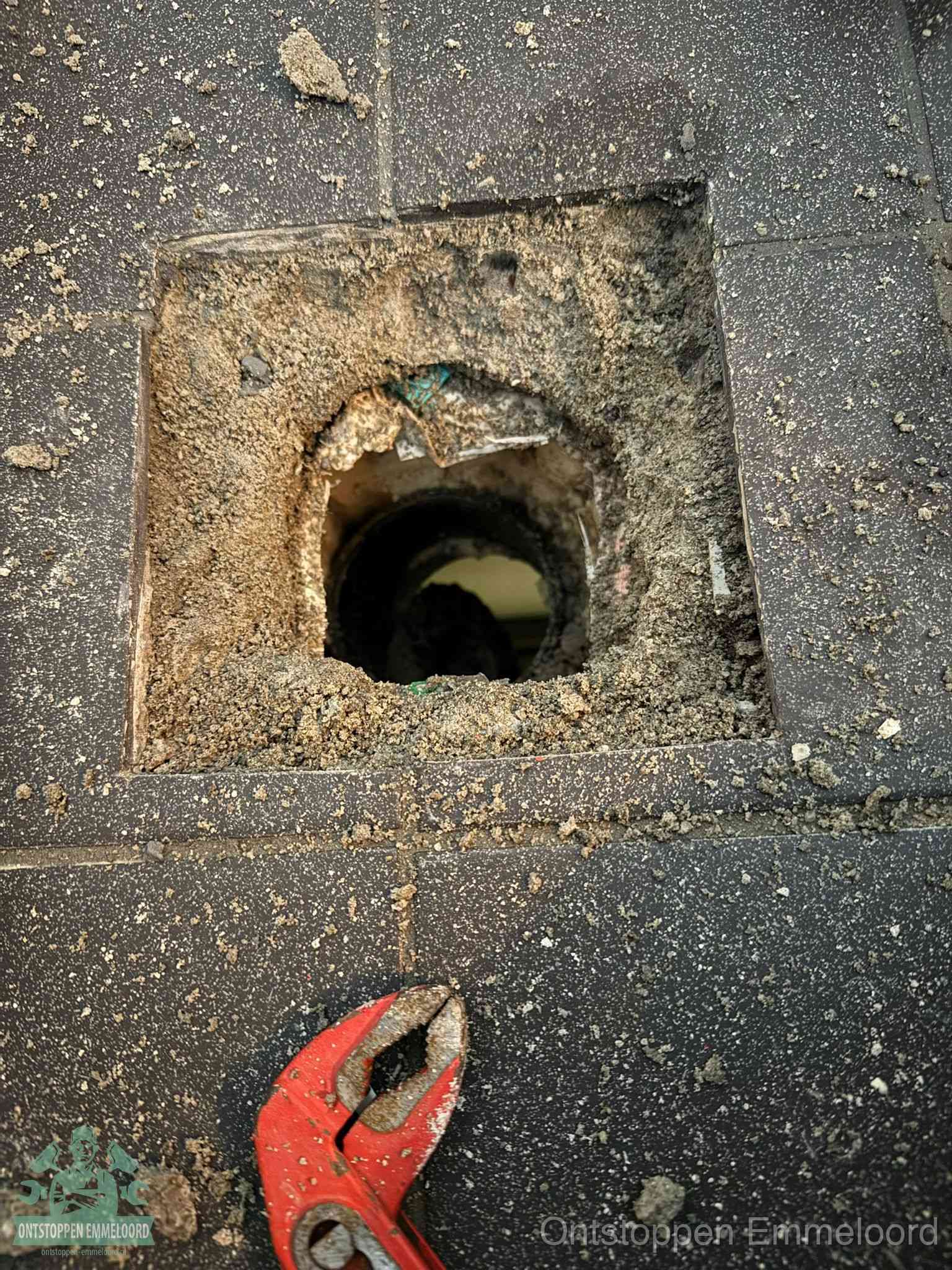 Een geopend rioolputje in een betontegelvloer met losgemaakt rooster en een zichtbare ronde afvoerbuis, het achterhalen waar de afvoerverstopping zit in Emmeloord