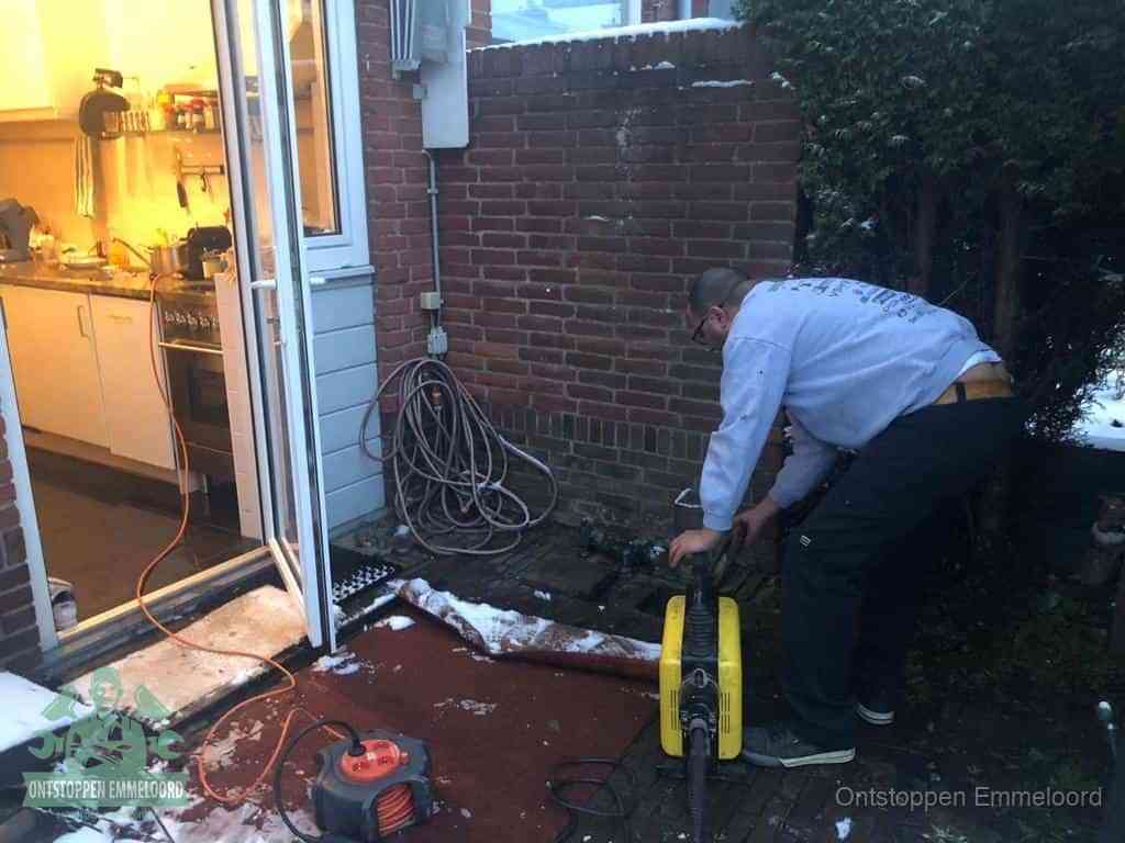 Een monteur werkt buiten bij een open riool-/grondput met een elektrische ontstoppingsmachine om een verborgen afvoerprobleem op te sporen in Emmeloord