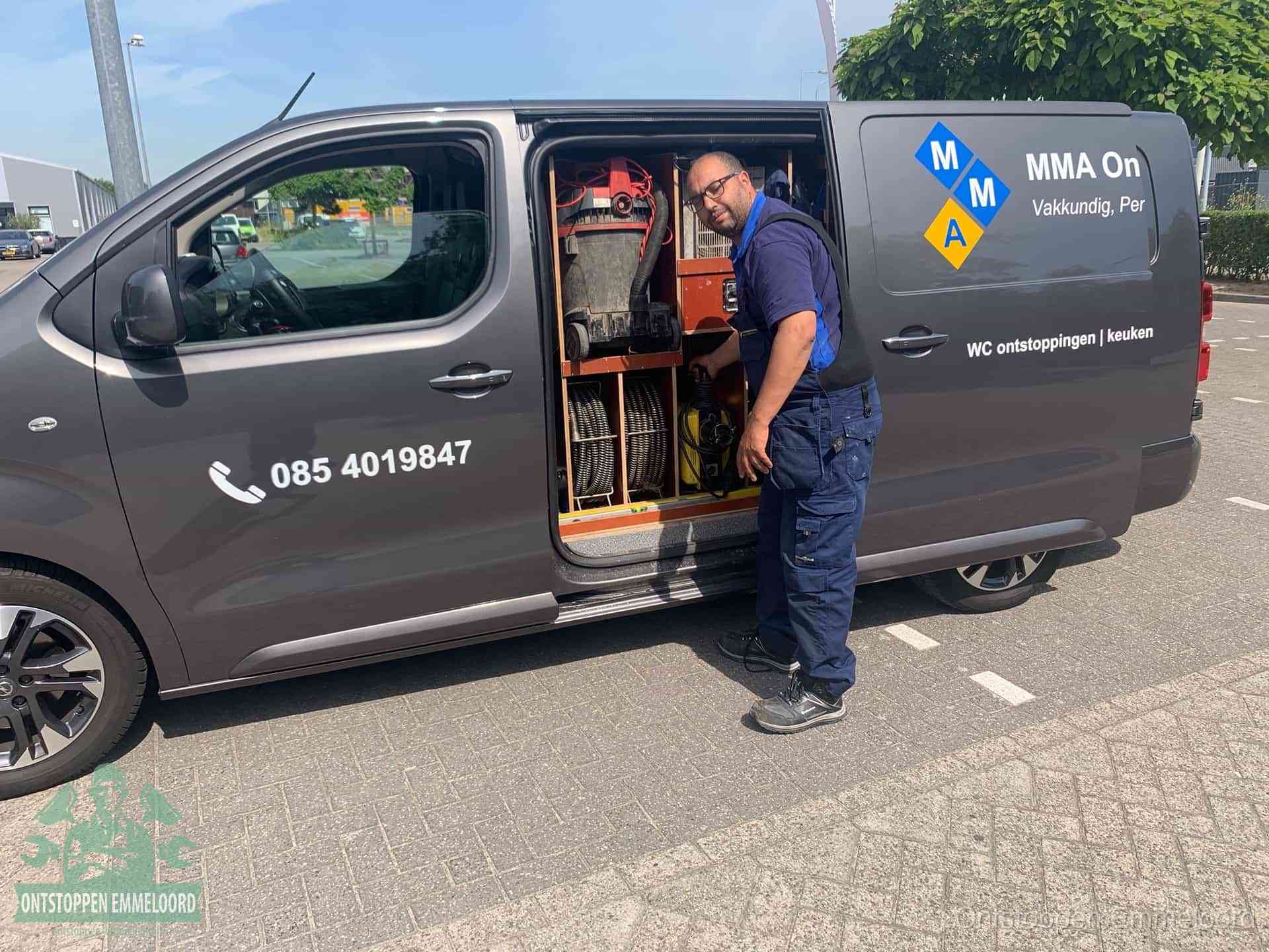Een monteur bij de open schuifdeur van zijn bedrijfsbus op een parkeerplaats, klaar om de oorzaak van terugkerende afvoerverstoppingen aan te pakken in Emmeloord