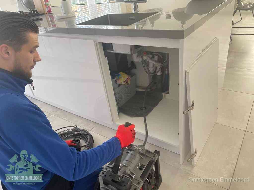 Monteur ontstopt met een veermachine een verstopte afvoer onder de gootsteen in Emmeloord