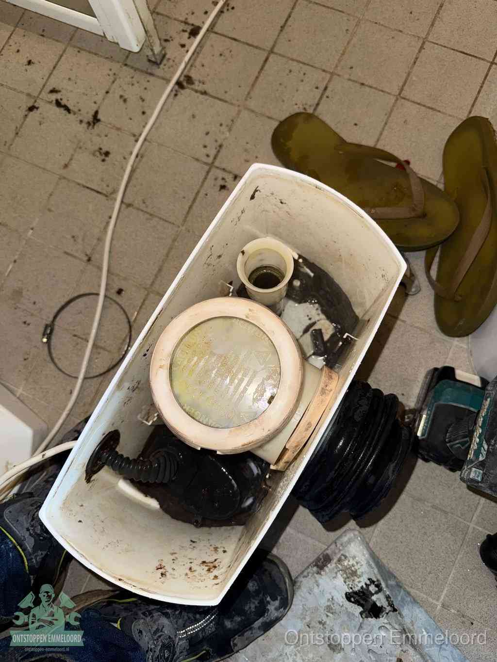 Een gedemonteerde toiletpot op de vloer met ontstoppingsveer en gereedschap ernaast, het verwijderen van een vastzittend voorwerp uit de wc in Emmeloord
