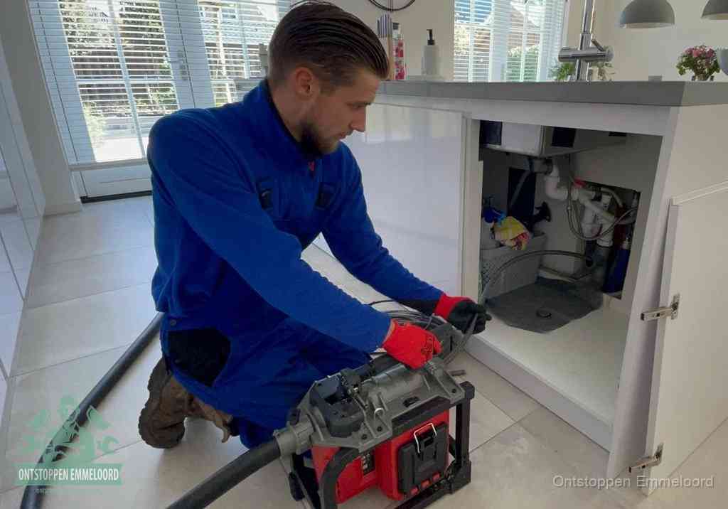 Een monteur voert een professionele elektrische ontstoppingsmachine in de afvoer onder de spoelbak tijdens het gootsteen ontstoppen in Emmeloord