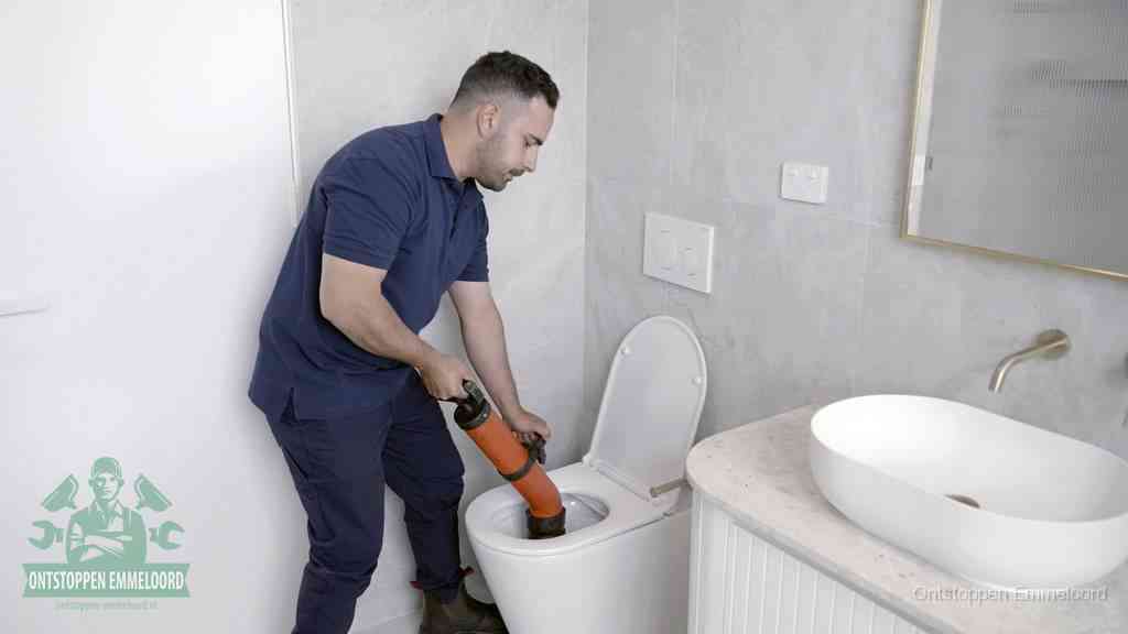 Een man gebruikt een handmatige luchtdruk-ontstopper in een modern betegeld toilet om zelf de wc te ontstoppen in Emmeloord